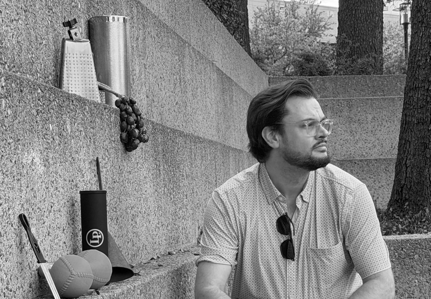 Taylor Dwyer seated on concrete steps beside a set of hand percussion — cowbell, metal shaker, egg shakers, and a tambourine