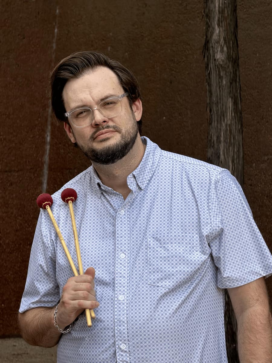 Taylor Dwyer holding a pair of vibraphone mallets against a rust-red wall